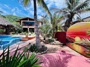 A resort with a swimming pool, palm trees, and a large mural.