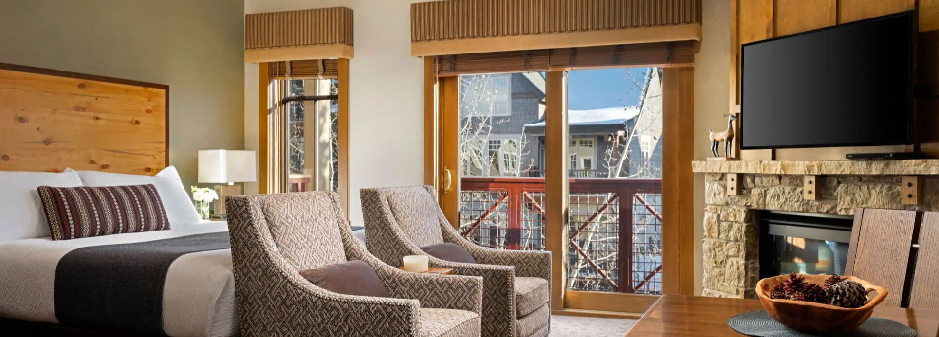 Ein Hotelzimmer mit einem Bett, zwei Sesseln, einem Fernseher, einem Kamin und Blick auf Gebäude.