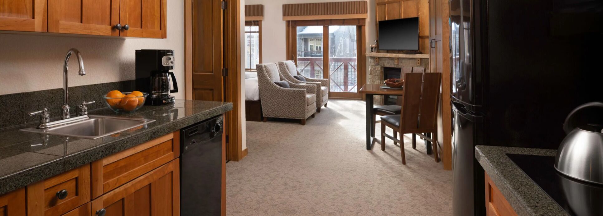 A kitchen with a dishwasher, a coffee maker, and a bowl of fruit. There is a dining area with a table and chairs, and a fireplace.