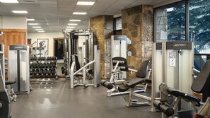 Ein Fitnessstudio mit unterschiedlichen Trainingsgeräten, darunter Kurzhanteln, Kraftgeräte und Bänke.