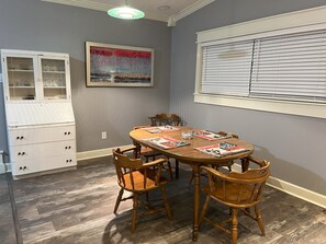 Un comedor con una mesa redonda de madera, cuatro sillas de madera, un armario blanco con puertas de cristal y un cuadro enmarcado en la pared.