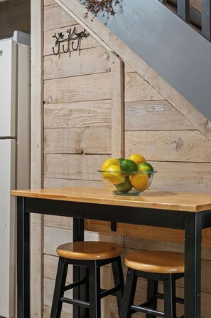 A kitchen area with a wooden wall, a glass bowl of fruit on a wooden table, and two black stools. - Updated Studio in Elkhorn Village, Sun Valley (Sun Valley)