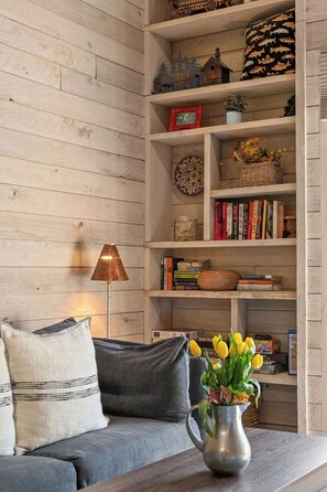 A living room with a grey sofa, a metal vase with flowers, and a wooden bookshelf with various items. - Updated Studio in Elkhorn Village, Sun Valley (Sun Valley)