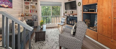 A spacious living room with a staircase, wooden walls, a large window, and a fireplace.