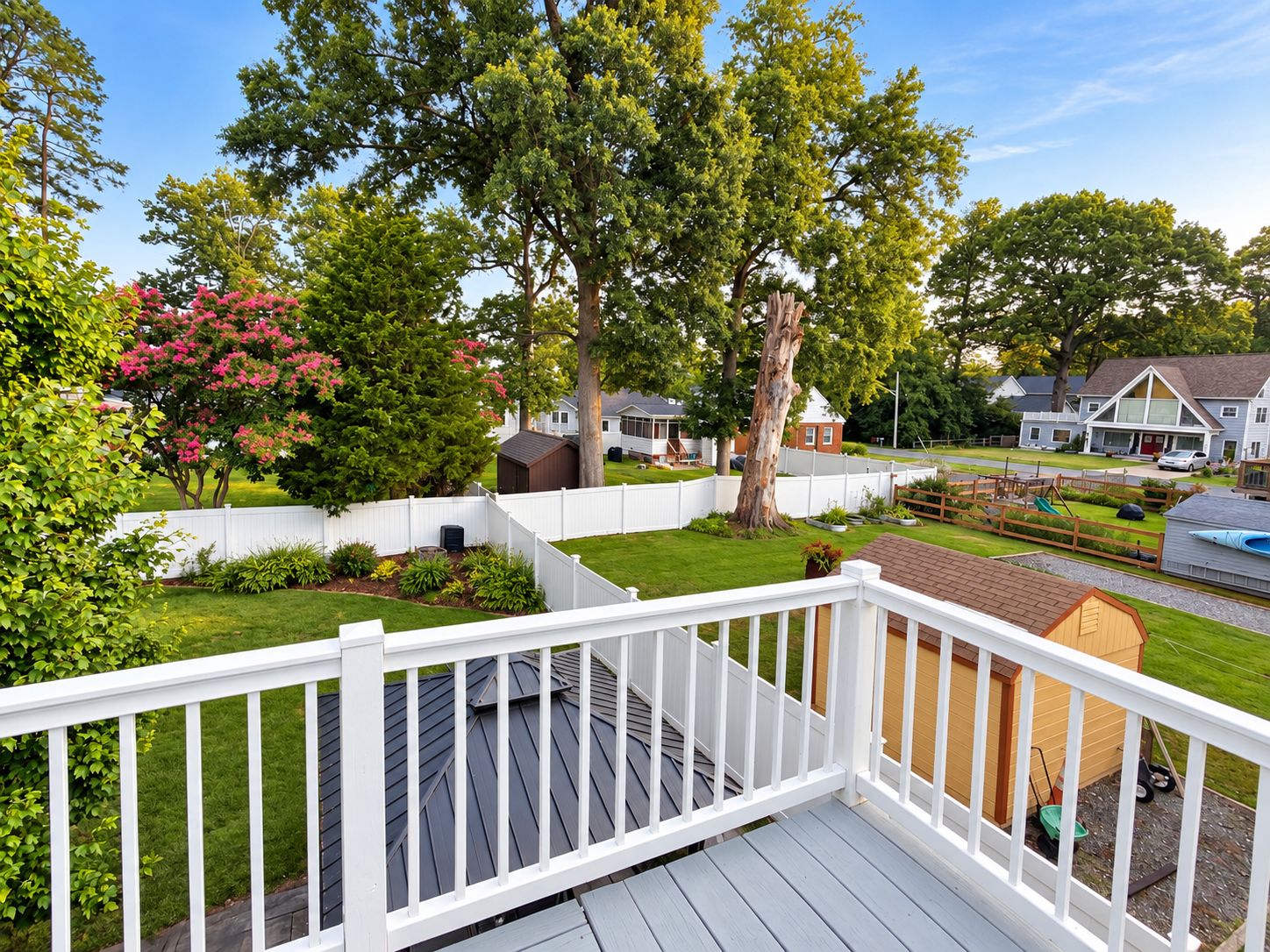 A residential backyard with a wooden deck, a fenced play area, and mature trees.