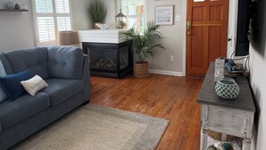 A living room with a gray sofa, a fireplace, wooden flooring, a door, and a wall-mounted TV.