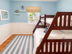 A room with a bunk bed, a window with a view, a striped rug, and wall decorations. - Rose Haven Coastal Cottage (North Beach)