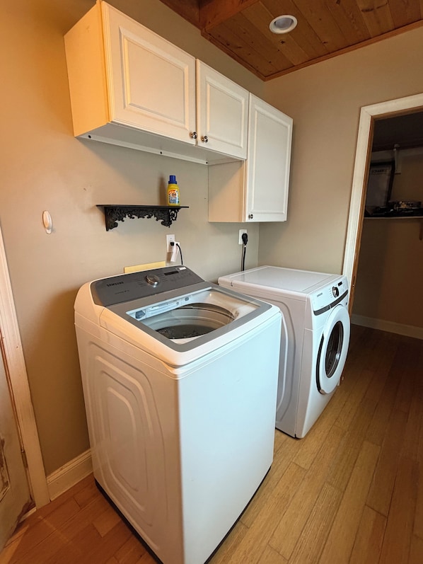 A laundry room with a washing machine and dryer, wooden cabinets above, and a shelf with a bottle.