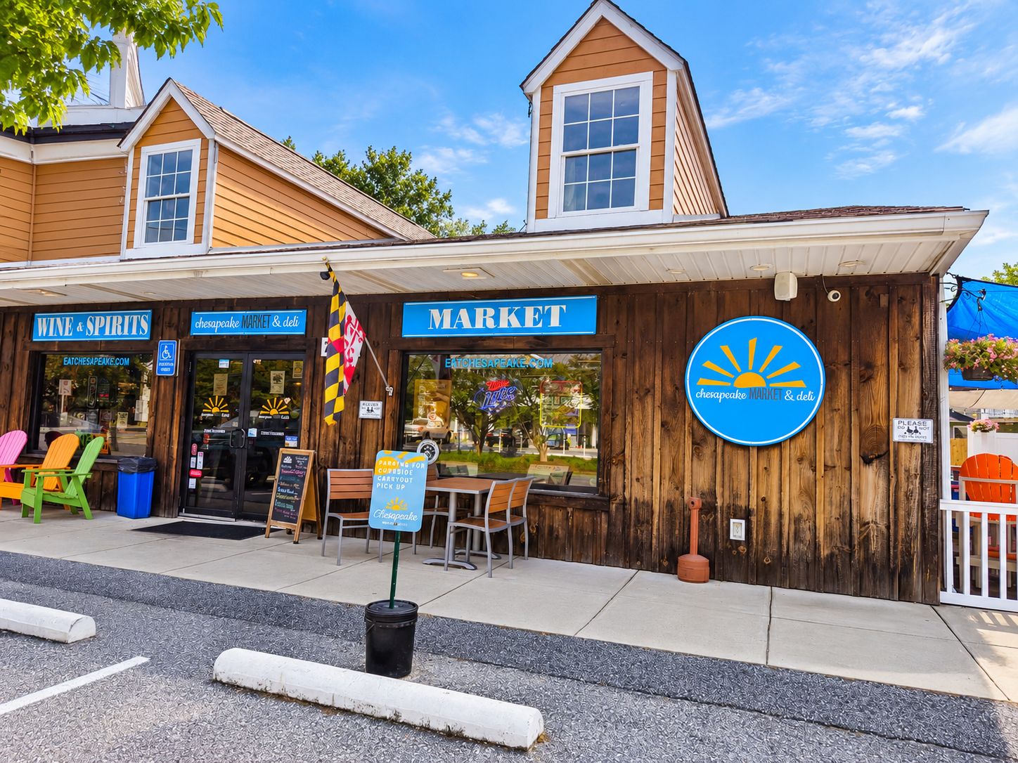 Un bâtiment en bois avec une enseigne indiquant « Chesapeake Market & deli », un petit espace extérieur aménagé avec des sièges et un drapeau.