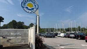 A sign for Herrington Harbour with a clear sky and parked cars in the background.