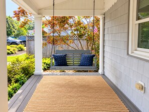 A porch with a swing, a wooden bench, and a doormat. - Rose Haven Coastal Cottage (North Beach)