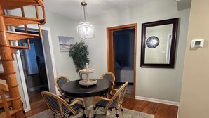 A dining area with a round table, four chairs, a chandelier, and a spiral staircase. - Rose Haven Coastal Cottage (North Beach)