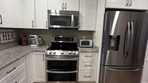 A modern kitchen with white cabinetry, stainless steel appliances, and a wooden floor.