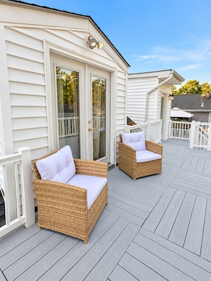 A covered outdoor area with two wicker chairs and a white door.