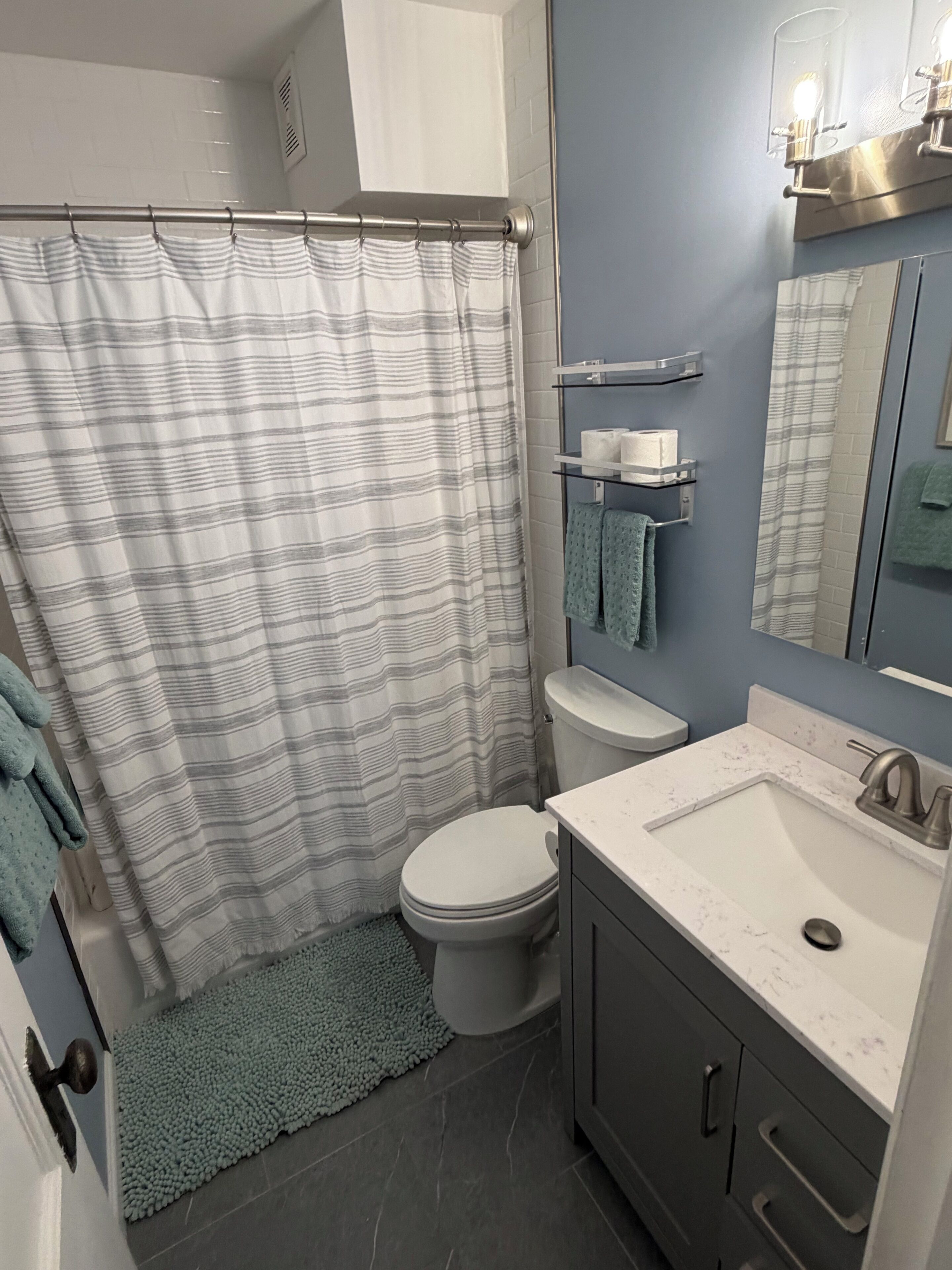 A bathroom with a shower curtain, toilet, sink, and towel rack.