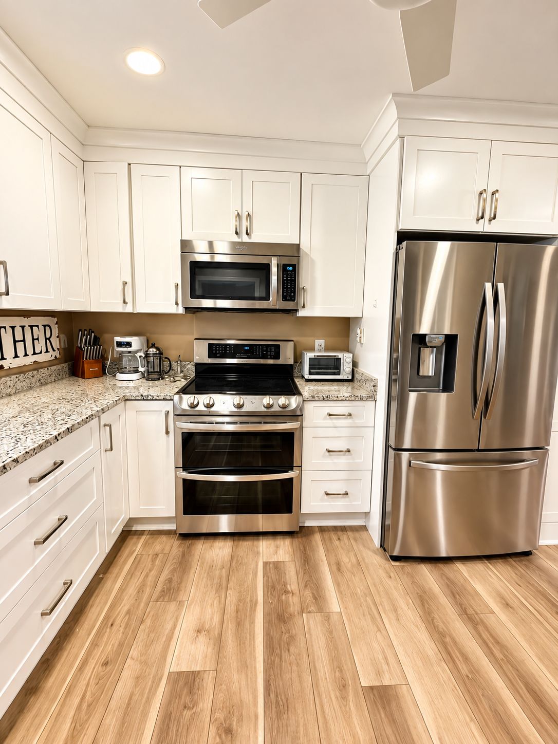A modern kitchen with stainless steel appliances, white cabinetry, and a wooden floor.