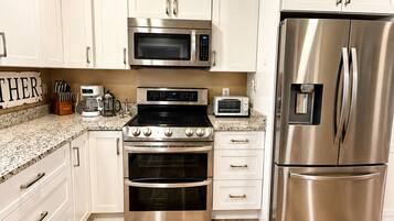 A modern kitchen with stainless steel appliances, white cabinetry, and a wooden floor.