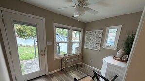 A room with a door leading outside, a ceiling fan, a bench, a radiator, and a window with a decorative panel. - Rose Haven Coastal Cottage (North Beach)