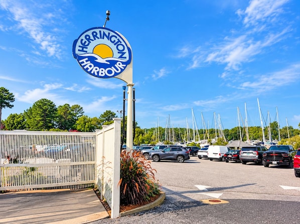A sign for Herrington Harbour with a clear sky and parked cars in the background.