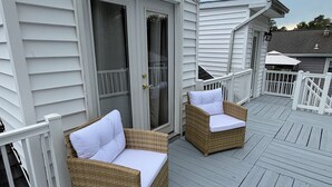 A covered deck with two wicker chairs and a white door. - Rose Haven Coastal Cottage (North Beach)