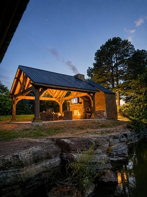 A covered outdoor area with a stone wall and a wooden deck, overlooking a body of water. - Waterfront Luxury Cabin with kayaking, paddleboarding, and fishing (Mulberry)