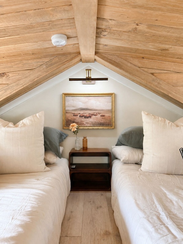 A bedroom with two beds, a nightstand with a vase, and a painting on the wall.
