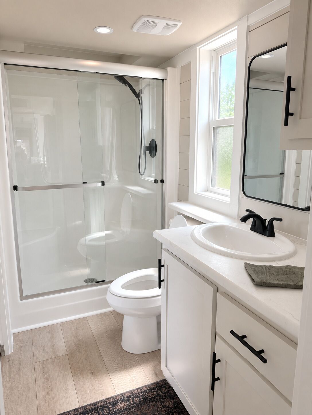 Une salle de bain moderne avec une douche à parois de verre, des toilettes blanches, un lavabo avec un miroir et un revêtement de sol en bois.