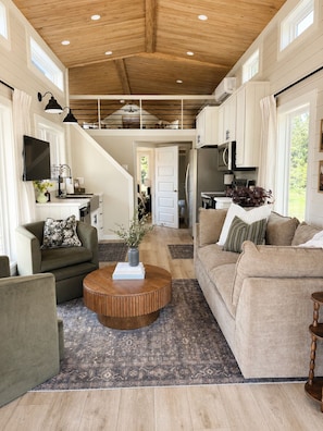 A spacious living area with a high ceiling, a central coffee table, sofas, and a television mounted on the wall. - Waterfront Luxury Cabin with kayaking, paddleboarding, and fishing (Mulberry)
