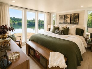 A bedroom with a large bed, a bench, a side table, and a view of a lake. - Waterfront Luxury Cabin with kayaking, paddleboarding, and fishing (Mulberry)