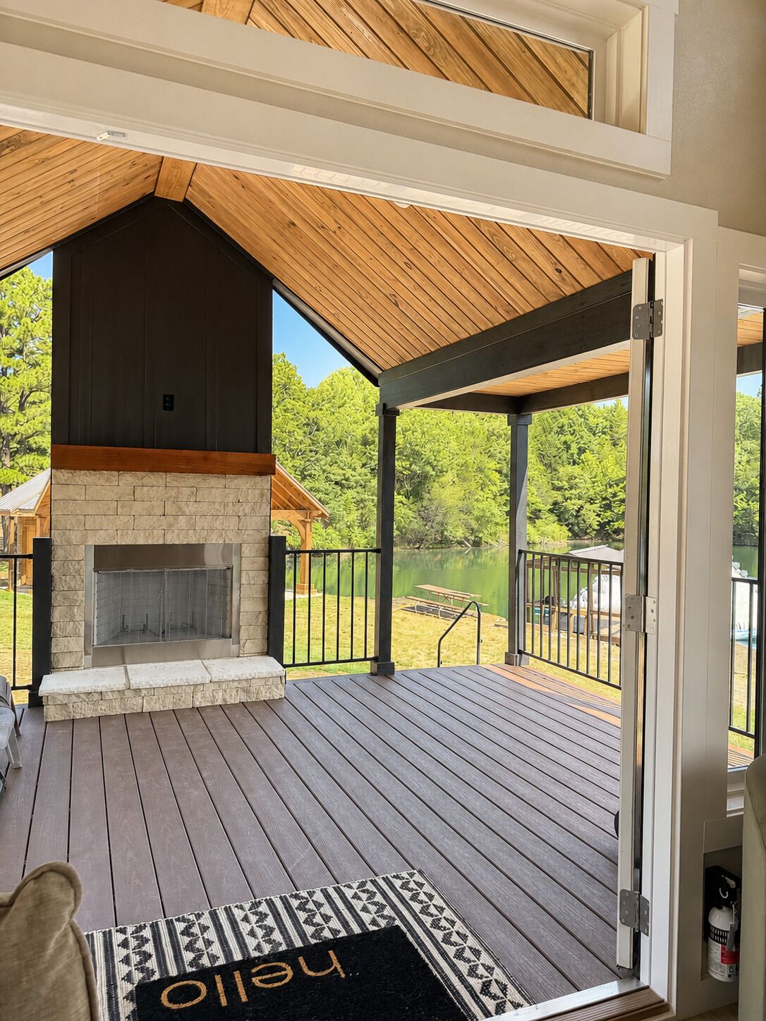 Une terrasse dotée d’une cheminée en pierre, d’un plafond en bois et offrant une vue sur un lac.