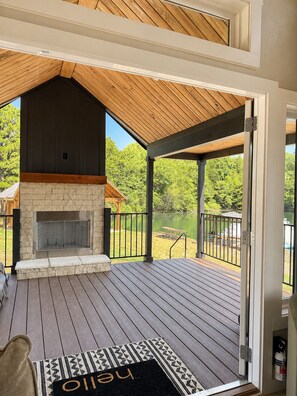 A deck with a stone fireplace, a wooden ceiling, and a view of a lake.