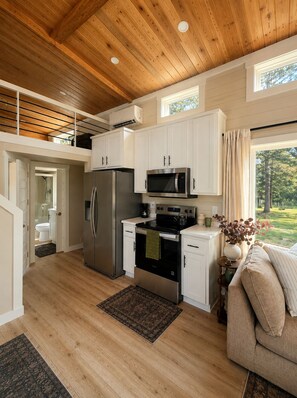 A modern kitchen with wooden ceiling beams, white cabinets, stainless steel appliances, and a view of the outdoors. - Waterfront Luxury Cabin with kayaking, paddleboarding, and fishing (Mulberry)