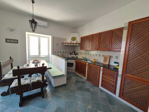 A compact kitchen with a dining area, featuring a bench, a stove, and wooden cabinets with a lattice design. - Casa Cachepot - Sweet Silvana (Ischia)