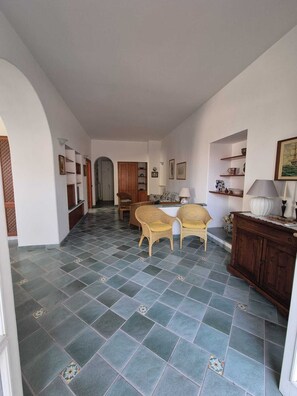 A spacious living area with a tiled floor, two wicker chairs, a wooden cabinet, and a dining table. - Casa Cachepot - Sweet Silvana (Ischia)