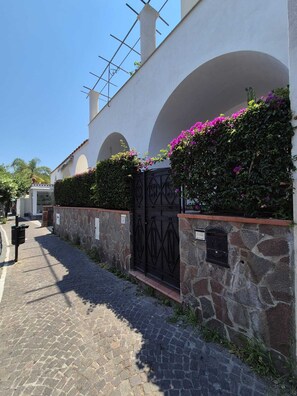 A cobblestone pathway leading to a building with a stone wall and a metal gate. - Casa Cachepot - Sweet Silvana (Ischia)