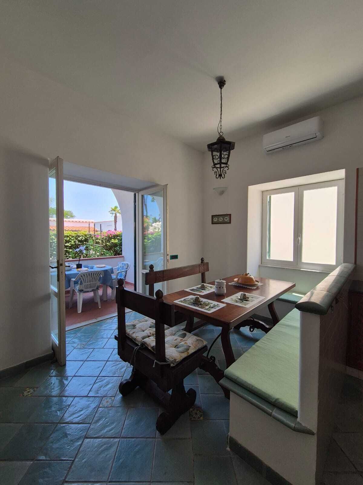 Una habitación con una mesa de comedor, sillas, un banco, una lámpara colgante y una ventana.