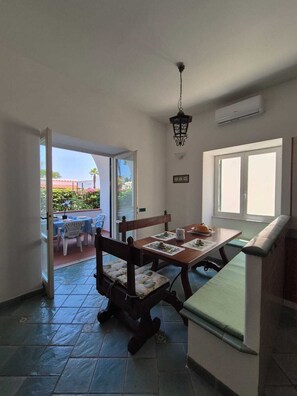 A room with a dining table, chairs, a bench, a hanging light fixture, and a window. - Casa Cachepot - Sweet Silvana (Ischia)