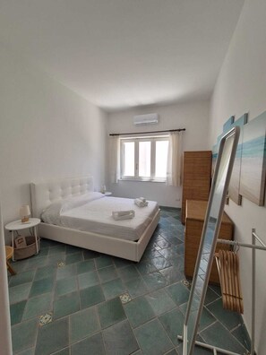 A bedroom with a bed, a window with curtains, a radiator, and a painting on the wall. - Casa Cachepot - Sweet Silvana (Ischia)