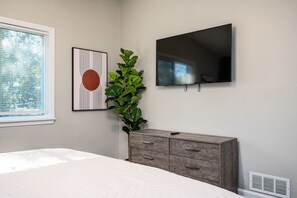 A bedroom with a bed, a dresser, a television mounted on the wall, and a window with blinds.