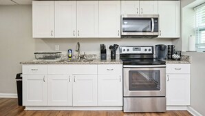 A modern kitchen with white cabinets, a stainless steel oven, a microwave, and a coffee maker. - Stylish 5BR Retreat Near Airport & Downtown (Atlanta)