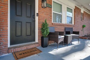 A brick house with a dark front door, a welcome mat, and outdoor wicker furniture.