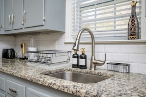 A kitchen with a granite countertop, stainless steel sink, and a window with blinds. - Stylish 5BR Retreat Near Airport & Downtown (Atlanta)