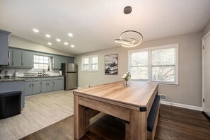 A modern kitchen with grey cabinets, a stainless steel refrigerator, and a wooden dining table with a vase of flowers. - Stylish 5BR Retreat Near Airport & Downtown (Atlanta)