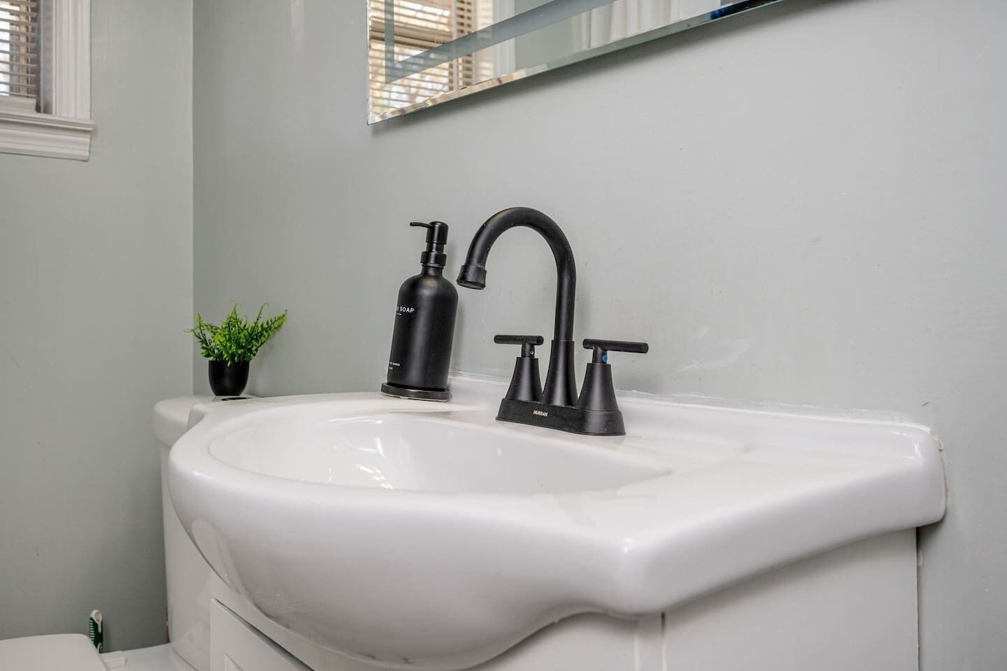 A bathroom with a white sink, black faucet, and soap dispenser.