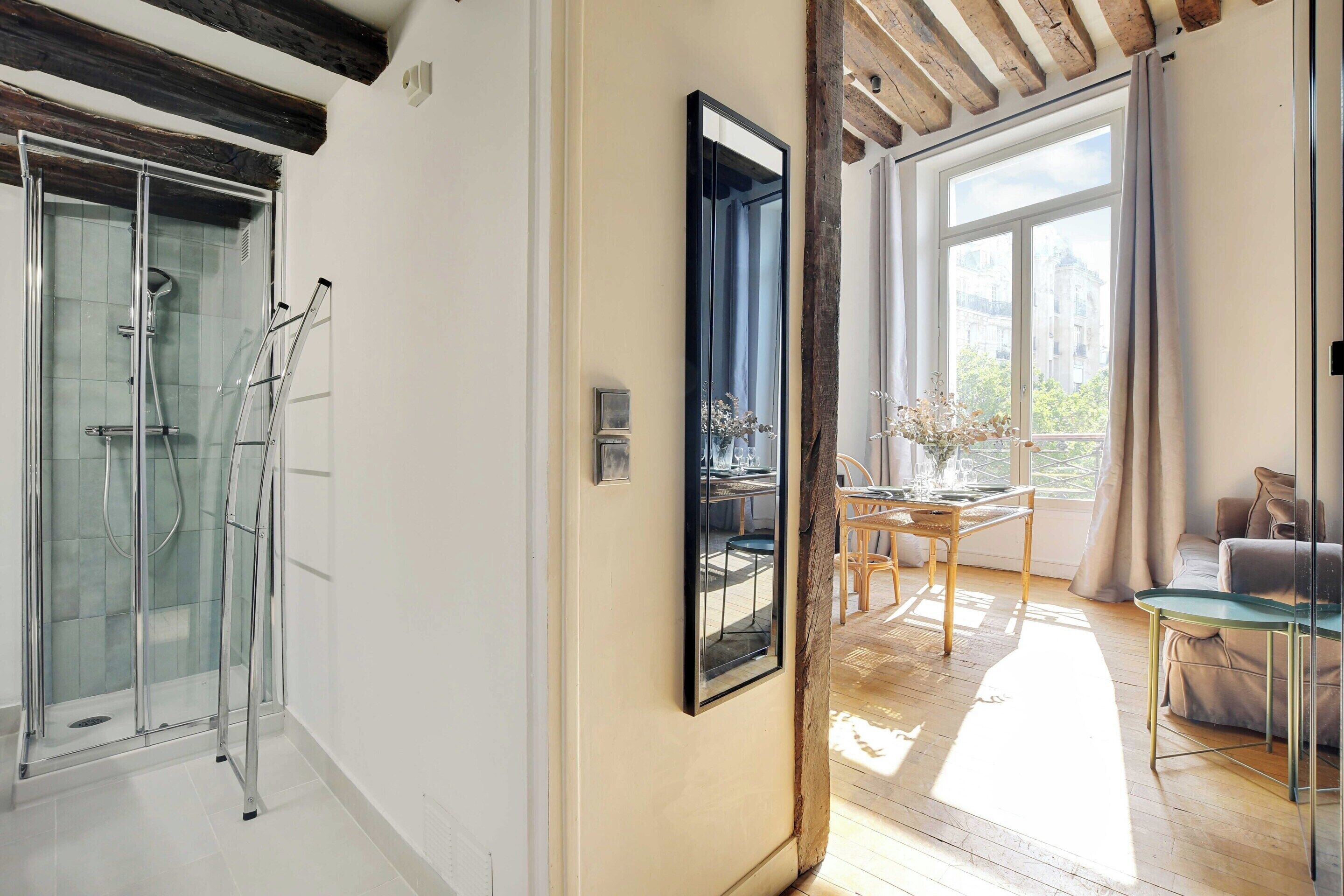 Un interior moderno con ducha de vidrio, comedor con luz natural y vistas a la ciudad.