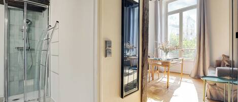 A modern interior with a glass shower, a dining area with natural light, and a view of the city.