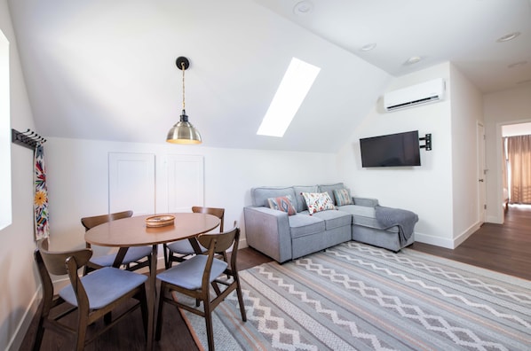 Un espacio moderno para vivir con comedor, sofá, televisor montado en la pared y una lámpara de techo.