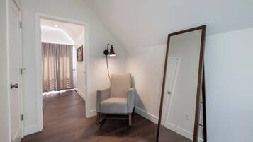 Una habitación con piso de madera, una silla, un espejo y una puerta que da a otra habitación.