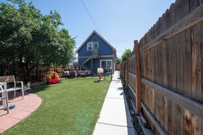 A backyard with a wooden fence, a basketball hoop, and a play area with a slide and a swing set.