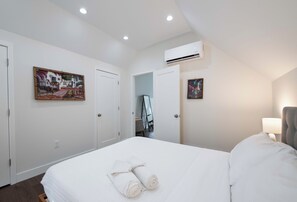 Una habitación de hotel con una cama, un cuadro, un equipo de aire acondicionado y una puerta que da a otra habitación.